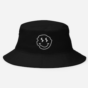 May include: Black bucket hat with a white embroidered smiley face with wavy lines for eyes.