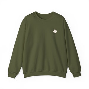 May include: Olive green sweatshirt with a small, off-white four-leaf clover embroidered on the left chest. The long-sleeved crew neck top is made of a soft material and is suitable for casual wear. The sweatshirt is a solid color.