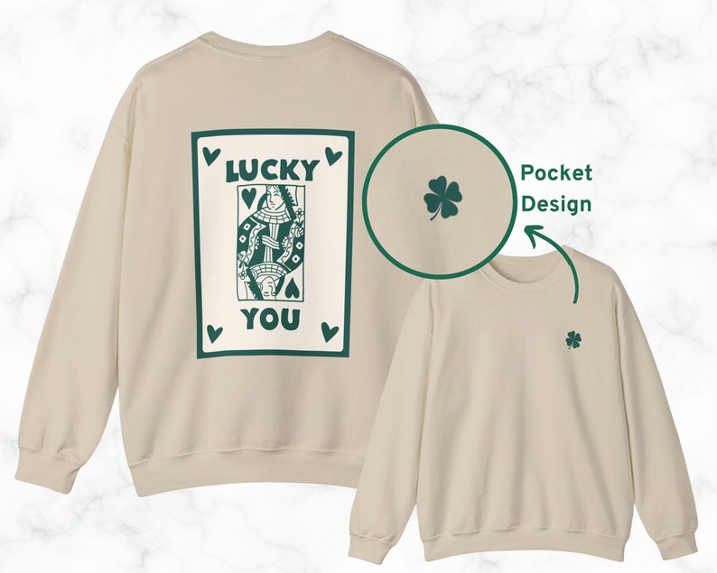 May include: A cream-colored sweatshirt with a green playing card design on the back that reads "LUCKY YOU." A small green four-leaf clover is on the front. The sweatshirt has a pocket design.