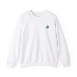 May include: A white crewneck sweatshirt with a small green four-leaf clover embroidered on the left chest. The sweatshirt has long sleeves and a classic, casual design. The fabric appears to be a soft, comfortable material, suitable for everyday wear.