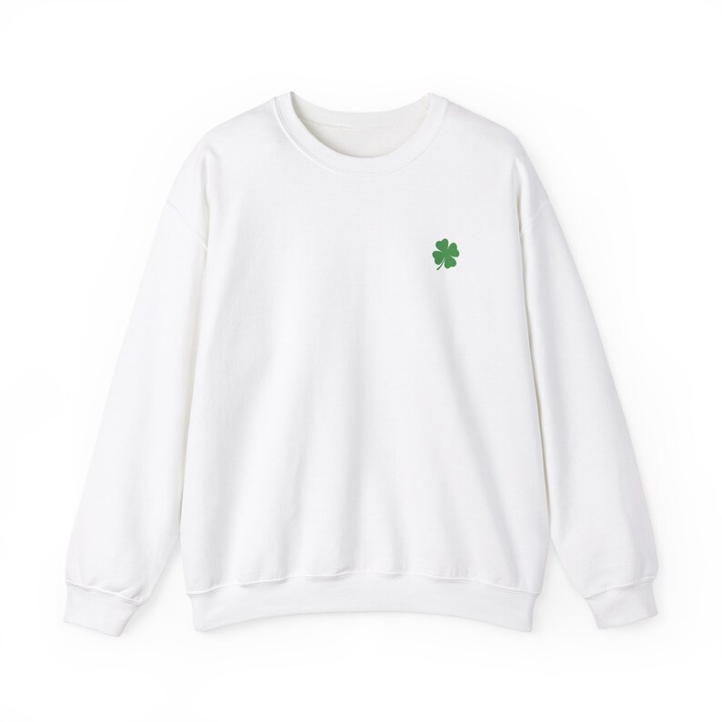 May include: A white crewneck sweatshirt with a small green four-leaf clover embroidered on the left chest. The sweatshirt has long sleeves and a classic, casual design. The fabric appears to be a soft, comfortable material, suitable for everyday wear.