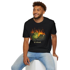 May include: Black t-shirt featuring a cartoon frog wearing a headset and sitting in front of a computer, with flames in the background. The text "go ahead." is printed below the frog.