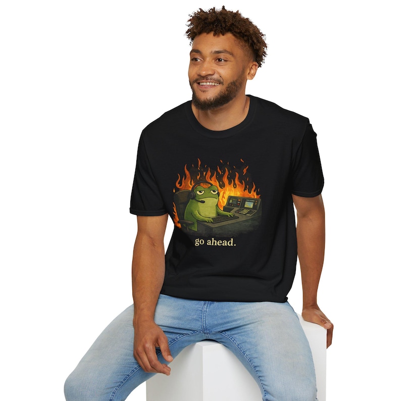 May include: Black t-shirt featuring a cartoon frog wearing a headset and sitting in front of a computer, with flames in the background. The text "go ahead." is printed below the frog.