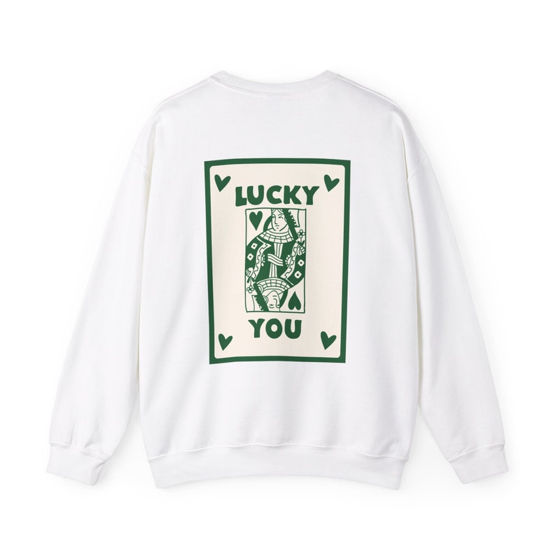 May include: White sweatshirt with a green and cream-colored playing card design on the back. The card features a queen illustration and the words "LUCKY YOU" in green. Small green hearts surround the card.