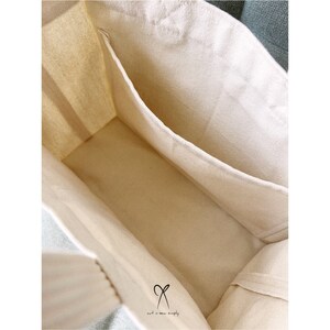 May include: A white canvas tote bag with a single interior pocket. The bag is unlined and has a natural cotton feel.