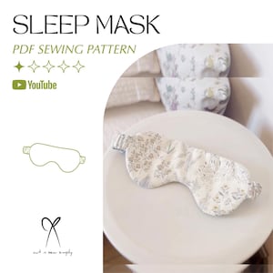 Puede incluir: Una máscara para dormir con estampado floral y correas elásticas, colocada sobre una superficie blanca. La máscara es blanca con un diseño de hojas y flores beige y grises. El texto en la imagen dice "SLEEP MASK" y "PDF SEWING PATTERN".