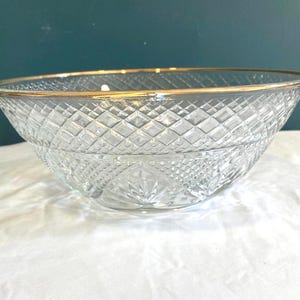 May include: A clear glass bowl with a diamond pattern and a gold rim. The bowl is sitting on a white surface. The bowl is a decorative piece.