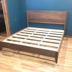 May include: A wooden bed frame with a headboard. The bed frame is made of dark brown wood and has a slatted base. The headboard is rectangular and made of the same wood. The bed frame is approximately 80 inches long and 60 inches wide.