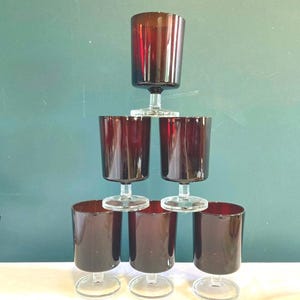 May include: A pyramid of six dark red wine glasses with clear stems and bases. The glasses are arranged in a stacked formation, with one glass at the top, two in the middle, and three at the bottom. The glasses have a cylindrical shape.