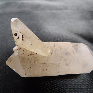 May include: A clear quartz crystal cluster with a prominent, angled point. The crystal has a translucent appearance with brown inclusions and a slightly rough texture. The overall shape is geometric and natural.