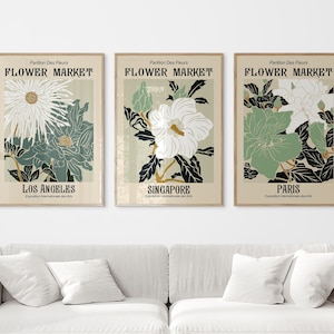 May include: Three vintage-style posters with floral illustrations and the text "FLOWER MARKET" in a bold, black font. Each poster features a different flower and city: Los Angeles, Singapore, and Paris. The posters have a beige background with a subtle texture.