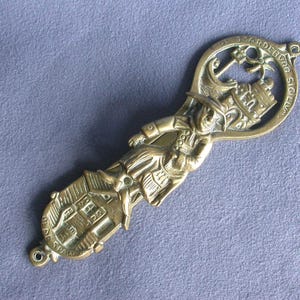 May include: Brass doorstop featuring a figure of a person holding a building with the text "Old St. Andrews Siglum" on the top.