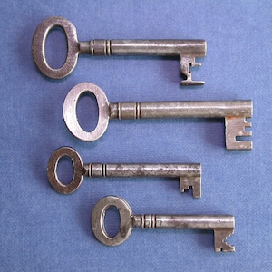May include: Four antique keys of varying sizes, with intricate designs on the keyhole and the end of the shaft, arranged vertically on a blue surface.