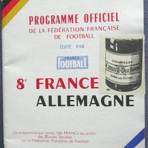 May include: A vintage French football program with red, black, yellow, and blue accents. The program features the text "PROGRAMME OFFICIEL" and "8e FRANCE ALLEMAGNE." A small black and white image of a champagne bottle is also present.