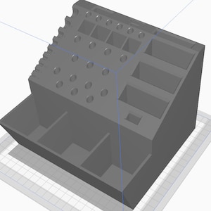 May include: A gray plastic organizer with multiple compartments and slots. The organizer has a large compartment at the bottom and several smaller compartments on the sides. There are also several round holes on the front of the organizer.