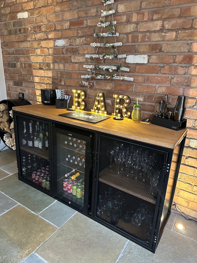 Puede incluir: Un bar de metal negro con una tapa de madera y puertas de vidrio. El bar tiene estantes para guardar botellas y vasos. El bar est&aacute; decorado con una cadena de luces que deletrea "BAR".