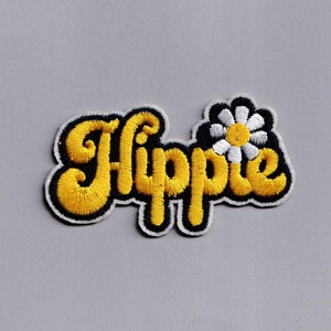 Może przedstawiać: Żółta naszywka haftowana z napisem "Hippie" w retro czcionce i białym stokrotkiem z żółtym środkiem.