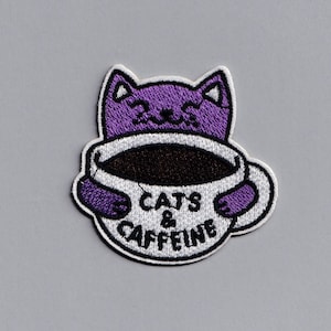 Op de afbeelding: Gestikt patch met een paarse kat die een witte koffiemok vasthoudt met de tekst "Cats & Caffeine".