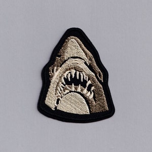 May include: A black and white embroidered patch of a shark's head with an open mouth and sharp teeth.
