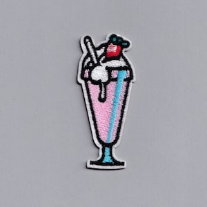 May include: An embroidered patch depicting a pink milkshake with a white whipped cream top, a red cherry, and a blue straw. The milkshake is in a tall glass with a black outline.