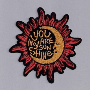 May include: Embroidered iron-on patch with a red and black sun and a crescent moon. The sun has the words "You are my sunshine" written in yellow.