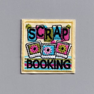 May include: A yellow embroidered patch with the words "Scrap Booking" in black lettering. The patch features three colorful photo frames with flowers.
