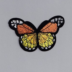May include: A yellow and orange embroidered butterfly patch with black outlines and white accents.