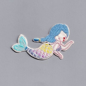 Può includere: Una toppa ricamata colorata con una sirena dai capelli blu, un guscio rosa e viola e una coda arcobaleno.