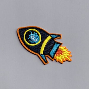 May include: A blue and yellow embroidered rocket patch with an orange flame. The rocket has a round window with a blue and white design inside.