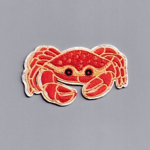 May include: Red embroidered iron-on patch of a crab with black eyes and a yellow outline.