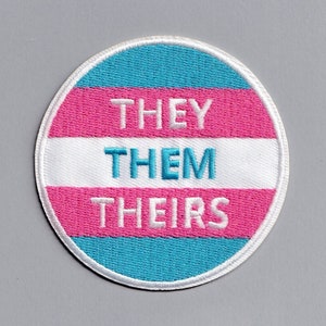 Peut inclure: Un patch rond brodé aux couleurs du drapeau de la fierté transgenre : bleu clair, rose et blanc. Le texte « THEY THEM THEIRS » est brodé en blanc sur le patch.