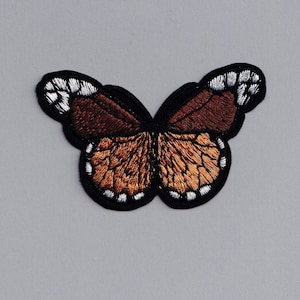 Puede incluir: Parche de mariposa bordada con borde negro. Las alas de la mariposa presentan tonos marrones y naranjas con detalles blancos. Este parche decorativo se puede planchar o coser en ropa o accesorios.