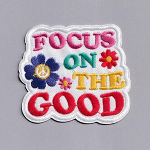 May include: White embroidered patch with the text "Focus on the good" in colourful letters. The patch is decorated with colourful flowers.