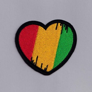 Peut inclure: Un patch en forme de cœur rouge, jaune et vert avec un contour noir. Le patch a un aspect vieilli avec des lignes noires qui le traversent.