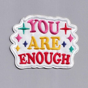 Op de afbeelding: Witte geborduurde patch met de tekst "YOU ARE ENOUGH" in kleurrijke letters. De patch is omringd door kleine kleurrijke sterren.