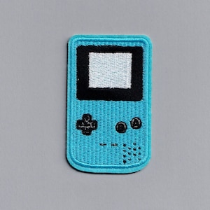 May include: A blue embroidered patch shaped like a handheld video game console. The screen is white and the buttons are black.
