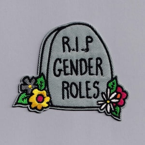 May include: A grey embroidered patch shaped like a tombstone with the text "RIP Gender Roles" and flowers on either side.