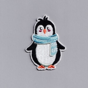 May include: A white penguin with black wings and a blue scarf. The penguin has a small orange beak and black eyes.