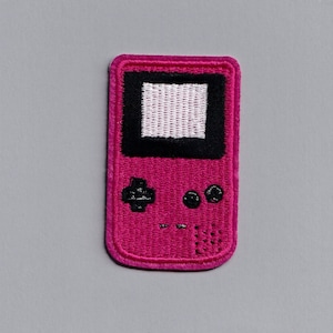 May include: An embroidered patch of a pink handheld video game console with a white screen and black buttons.