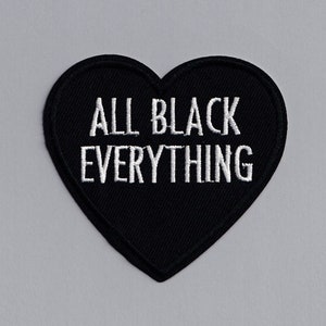 Könnte beinhalten: Schwarzer herzförmiger Patch mit weißer Stickerei, auf dem "ALL BLACK EVERYTHING" steht.