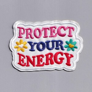 May include: White iron-on patch with a white background and colourful embroidered text that reads "PROTECT YOUR ENERGY". The text is surrounded by two colourful embroidered flowers.