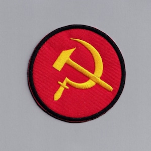 May include: A red circular patch with a black border, featuring a yellow hammer and sickle symbol.