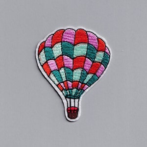 Op de afbeelding: Een kleurrijk geborduurd luchtballon-patch met rode, roze en groene strepen. De ballon heeft een witte omtrek en een rode mand.