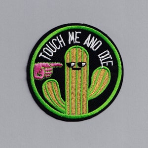Könnte beinhalten: Ein gestickter Kaktus-Patch in Grün und Gelb mit einer rosa Hand, die auf den Kaktus zeigt, und dem Text "Touch Me And Die".