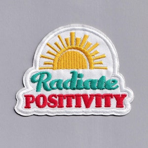 Könnte beinhalten: Weißer gestickter Aufnäher mit einer gelben Sonne und dem Text "Radiate Positivity" in Grün und Rot.