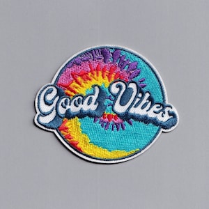 Peut inclure: Un patch rond blanc avec un motif tie-dye dans des tons de rose, jaune, bleu et violet. Les mots "Good Vibes" sont brodés en bleu sur le patch.