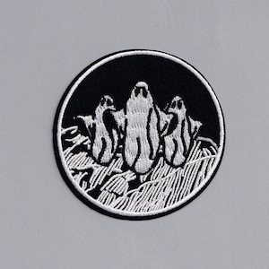 May include: A black and white embroidered patch featuring three ghosts in a circle. The ghosts are white and the background is black.