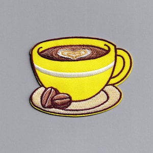 Puede incluir: Parche amarillo bordado para planchar con la imagen de una taza de café con un diseño en forma de corazón en el café y dos granos de café en un platillo.
