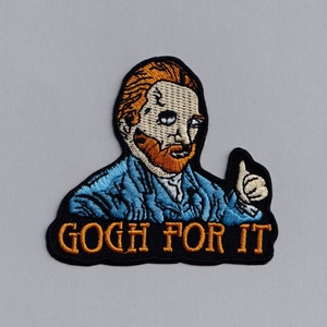 Op de afbeelding: Gestikte patch met een cartoon afbeelding van Vincent van Gogh met een blauw jasje en een oranje baard, die een duim omhoog geeft. De tekst "GOCH FOR IT" staat in oranje onder de afbeelding.
