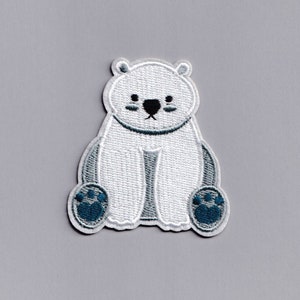 Puede incluir: Parche bordado blanco de un oso polar con huellas azules. El oso está sentado con las patas delante.